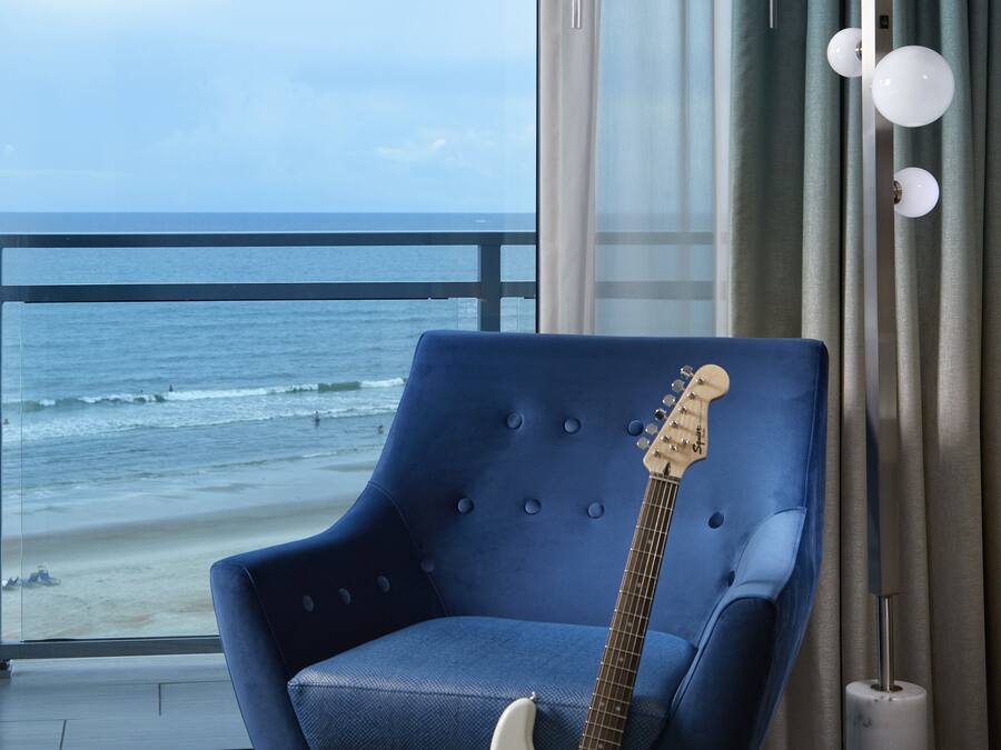 A room with a view of the ocean, a blue armchair, and a white electric guitar.