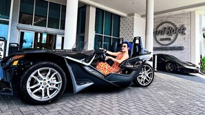 A person in a convertible car in front of a hotel with a sign that reads "Hard Rock Hotel Daytona Beach". - Hard Rock Hotel Daytona Beach (Daytona Beach)
