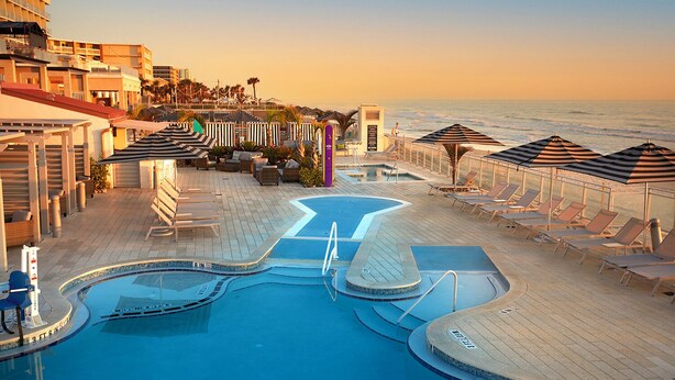 A resort pool area with multiple sun loungers and umbrellas, a central pool, and a view of the ocean. - Hard Rock Hotel Daytona Beach (Daytona Beach)