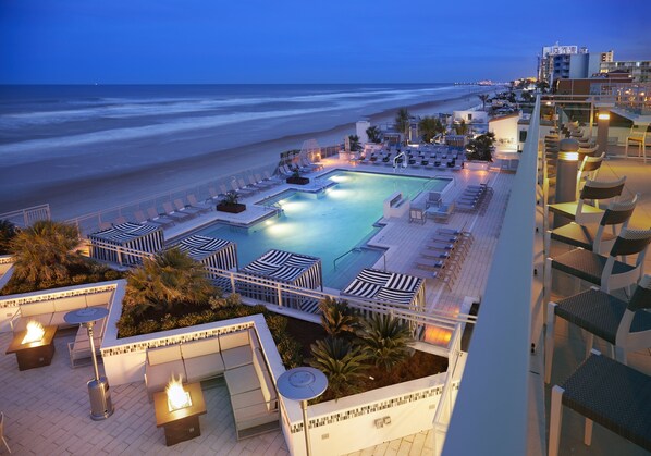 A rooftop pool with lounge chairs and a view of the beach at dusk. - Hard Rock Hotel Daytona Beach (Daytona Beach)