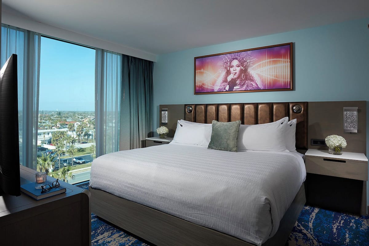 A hotel room with a large bed, a view of the city, and a painting on the wall.