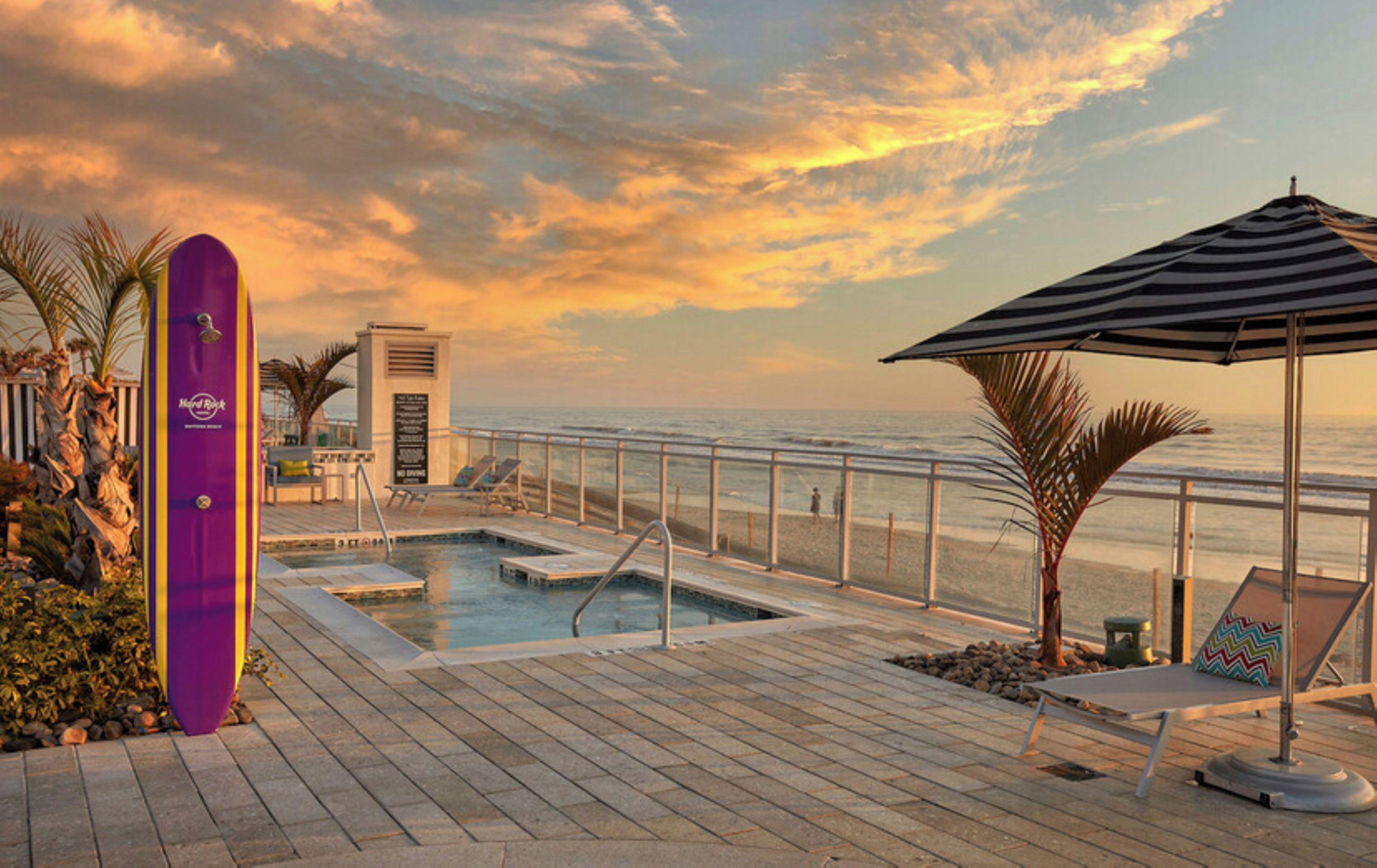 A poolside area with a lounge chair, a striped umbrella, and a view of the ocean.