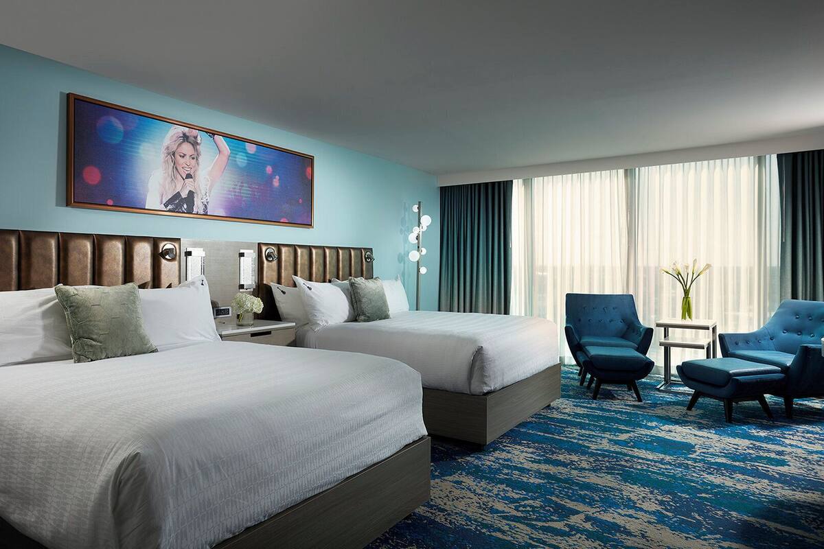 A hotel room with two beds, a large painting, a blue carpet, and a seating area with chairs.