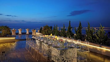 An outdoor dining area with a view of the sea, clear glass tables, and chairs.