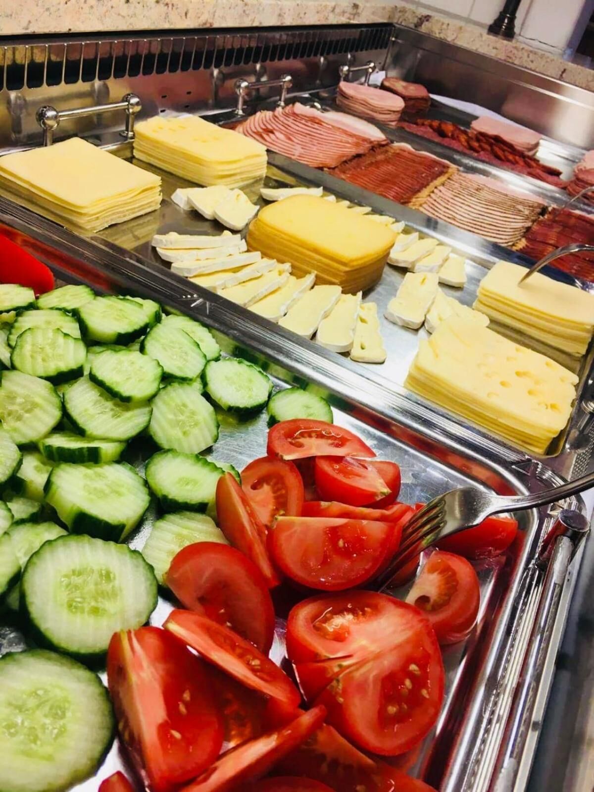 A buffet with various food items including sliced cucumbers, tomatoes, cheese, and meats.