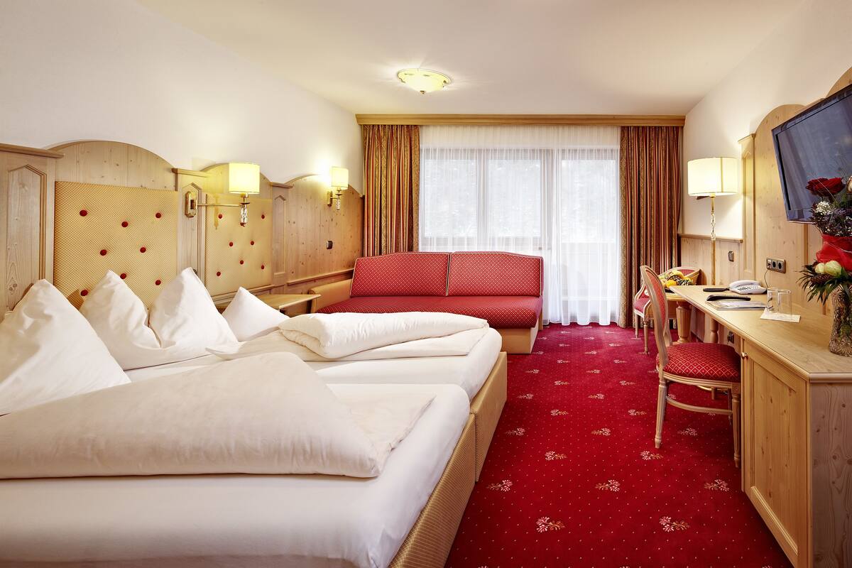 A hotel room with two beds, a desk, a chair, a television, and a large window with curtains.