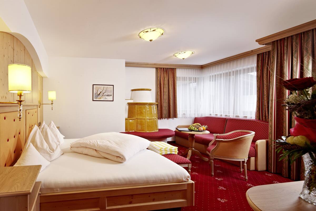 A hotel room with a bed, a seating area with a table and chairs, a large window with curtains, and a vase with flowers.