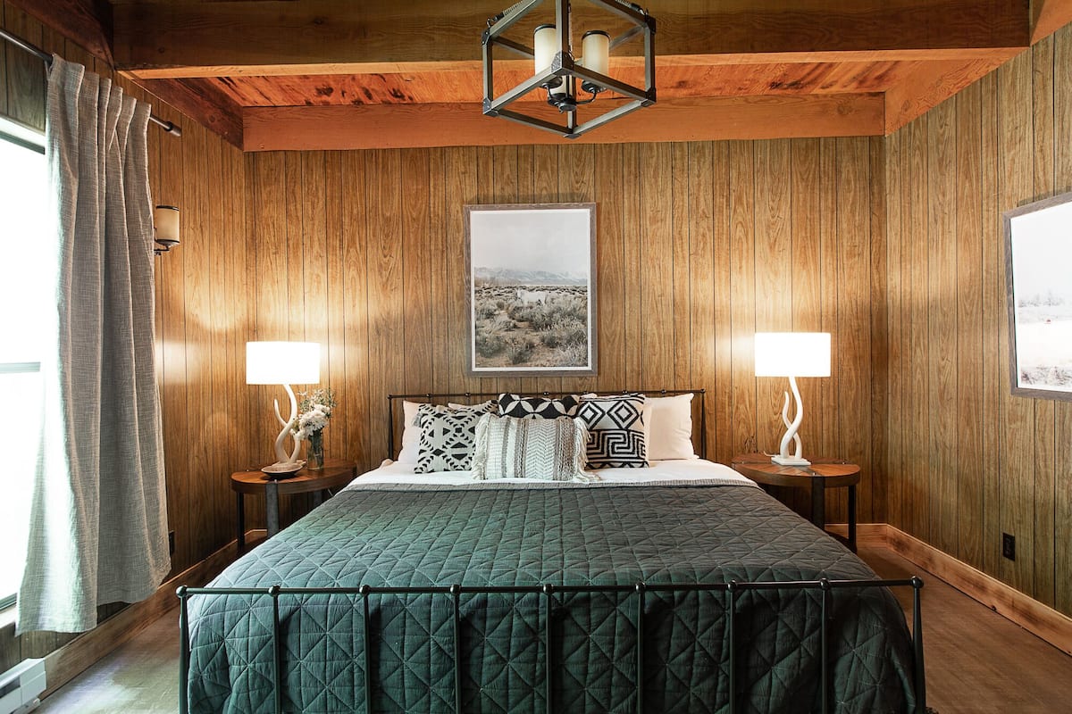 A wooden-paneled bedroom with a large bed, two bedside lamps, and a framed picture on the wall.