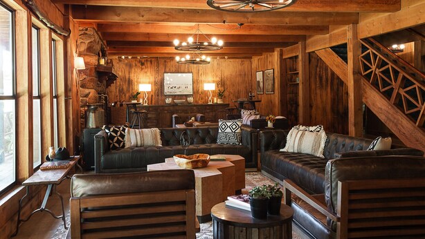 A rustic wooden interior with leather sofas, a stone fireplace, and a wooden staircase. - Greenhorn Ranch (Quincy)