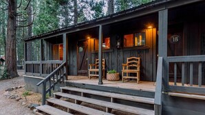 A rustic cabin with a wooden porch, two chairs, and a potted plant. - Greenhorn Ranch (Quincy)