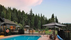 A swimming pool with lounge chairs and umbrellas, surrounded by a fence and a forested area. - Greenhorn Ranch (Quincy)