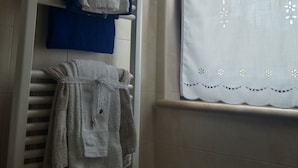 A bathroom with a towel rack holding multiple towels, a window with a decorative curtain, and a tiled wall. - I Tufi (Colonnella)
