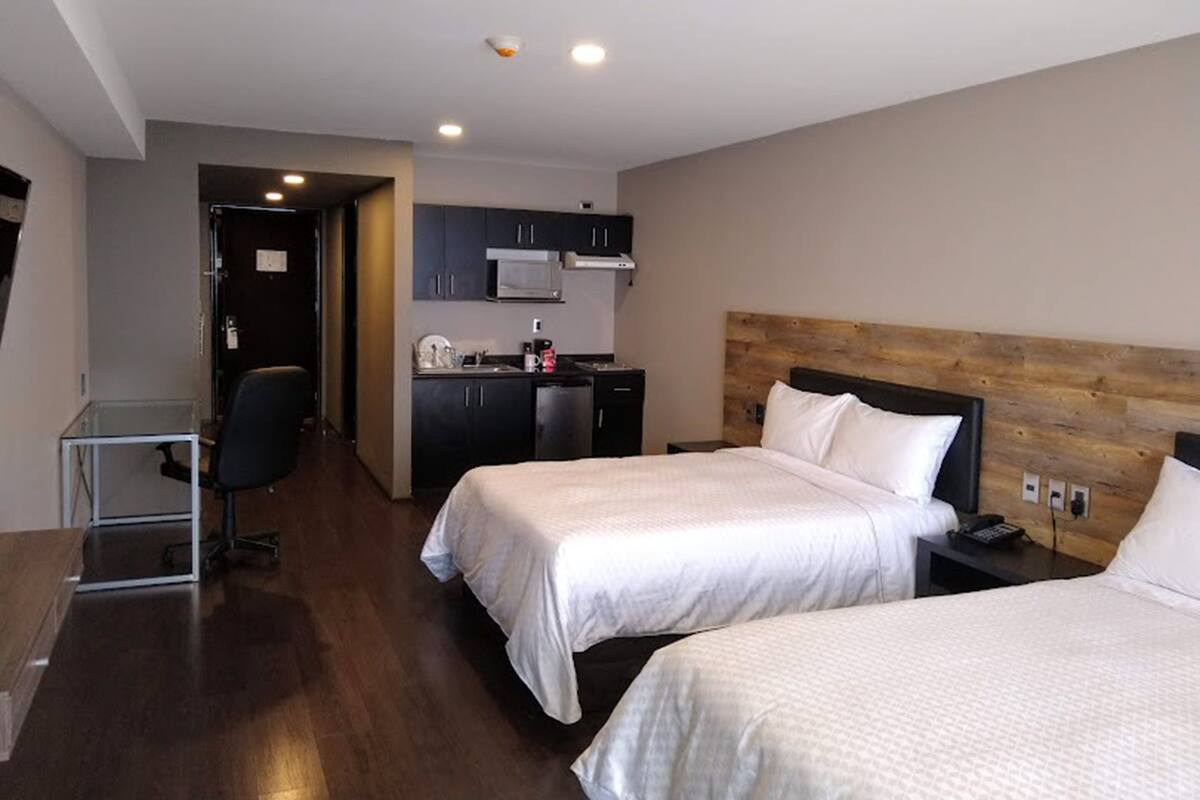 A hotel room with two beds, a kitchenette, a desk, and a chair.