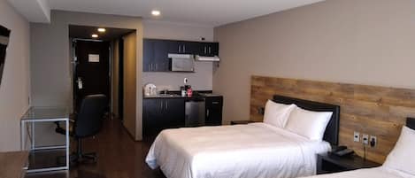 Habitación de hotel con dos camas, kitchenette, escritorio y una silla.