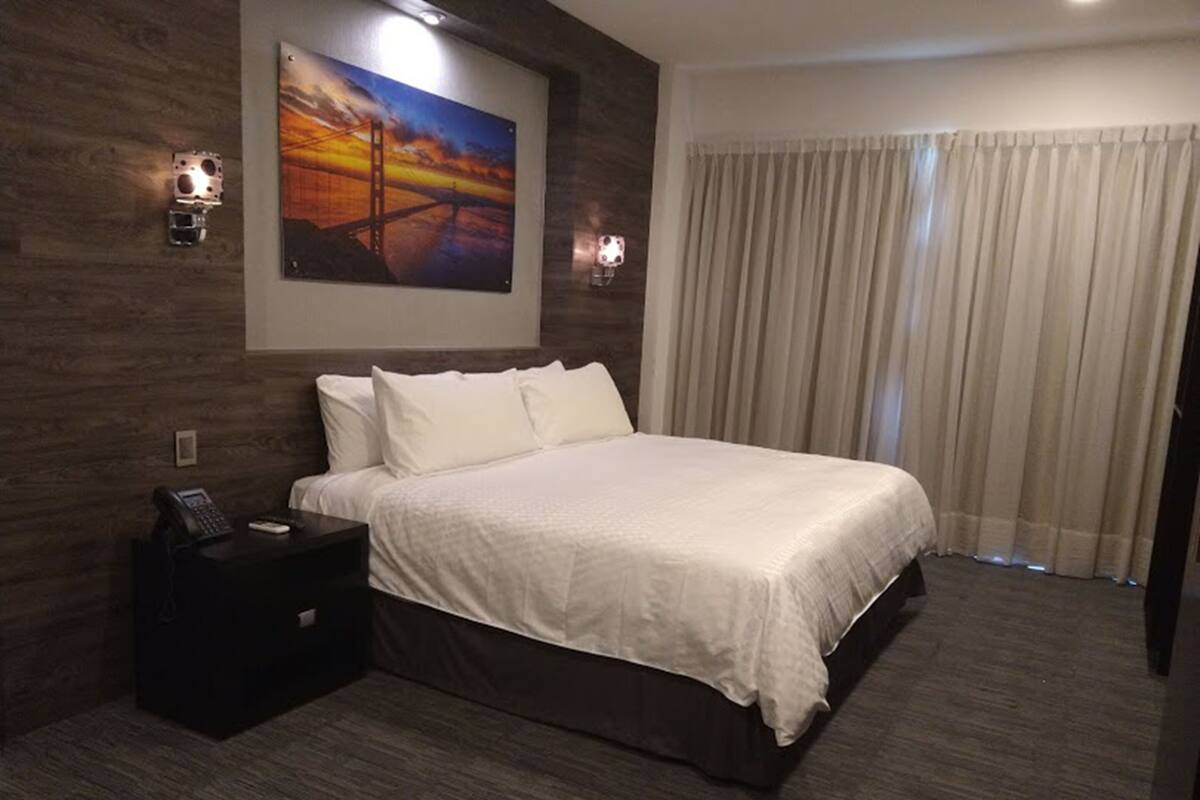 A hotel room with a large bed, a nightstand with a phone, and a painting of a sunset on the wall.