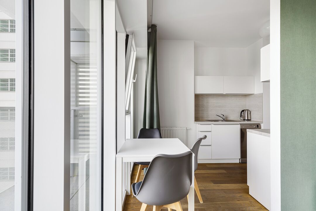 A modern kitchen with white cabinets, a black chair, and a window overlooking a cityscape.
