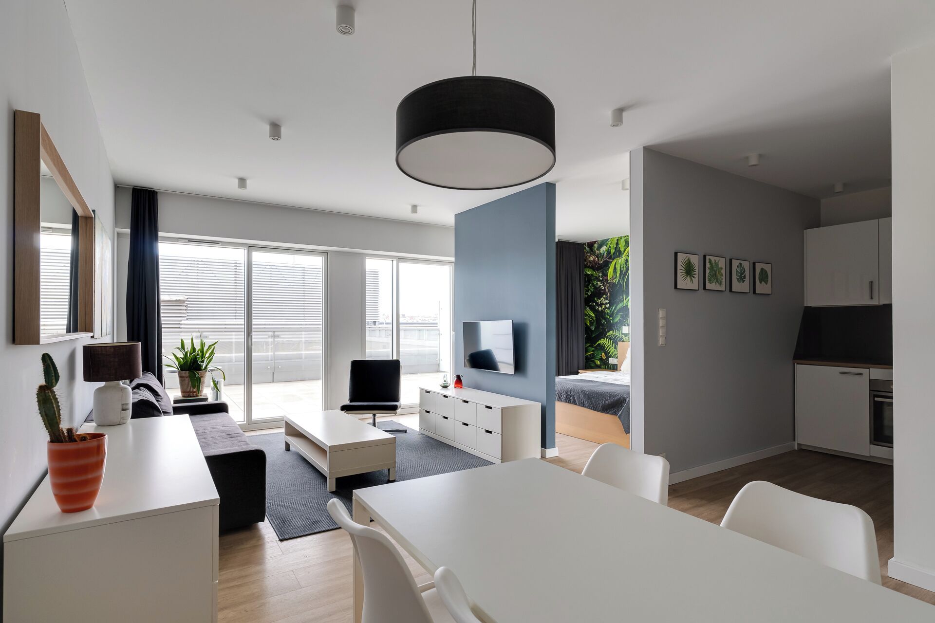 Un apartamento moderno con comedor, sala de estar con televisor, cocina y ventanas grandes con persianas.