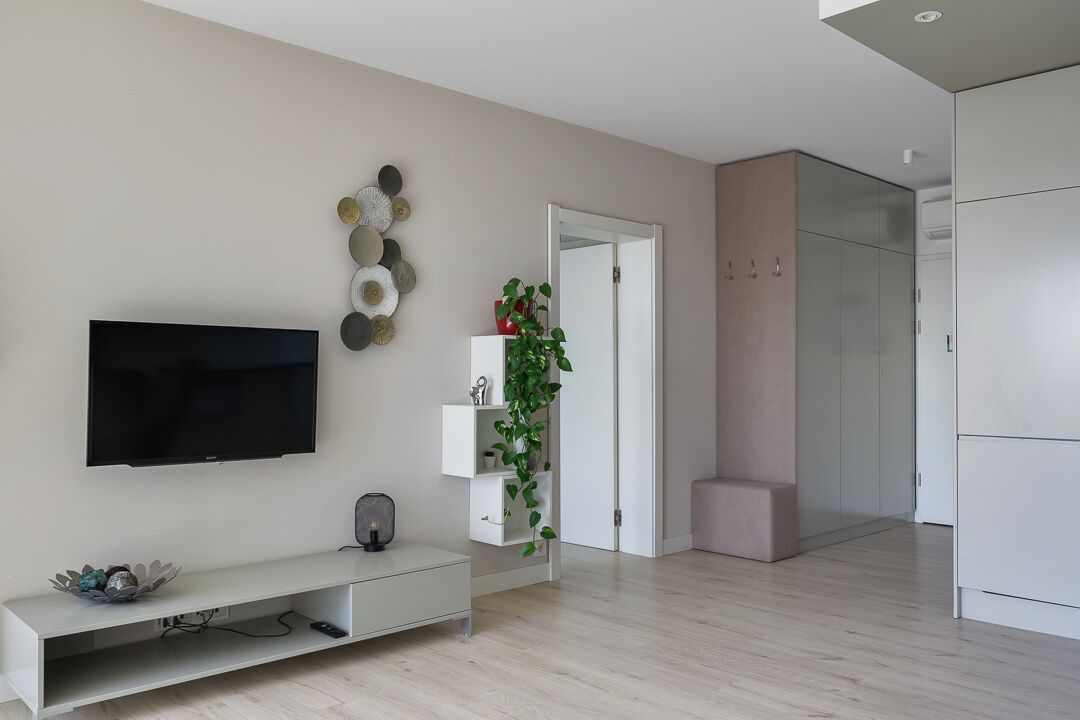 A modern living room with a flat-screen TV, a white entertainment unit, and a decorative wall piece.