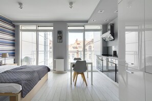 A modern bedroom with a large bed, a desk, and a chair. There is a view of the city through large windows. - Poznań Apartments Towarowa (Poznań)