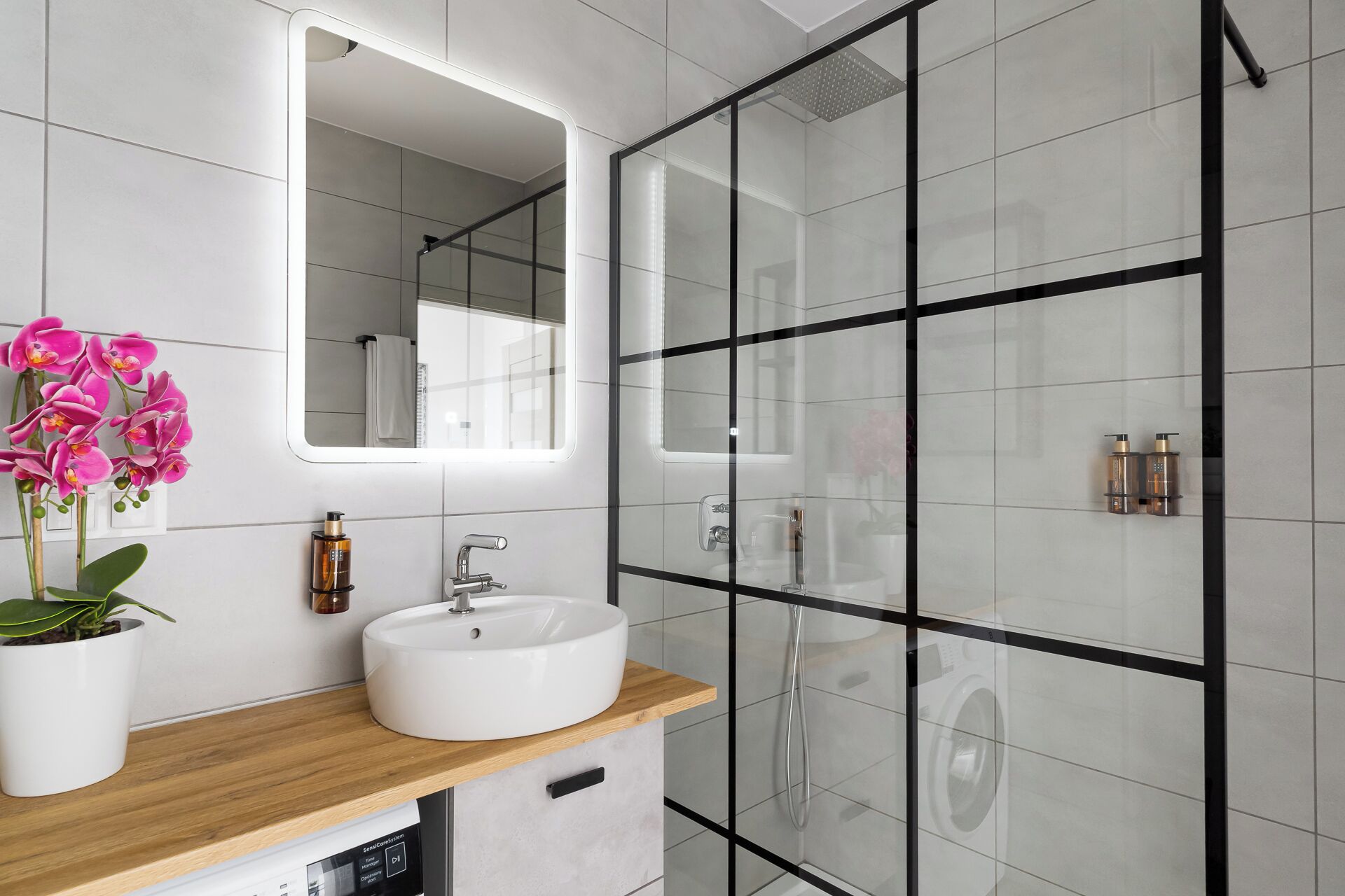 A modern bathroom with a white sink, a mirror, and a glass shower enclosure.
