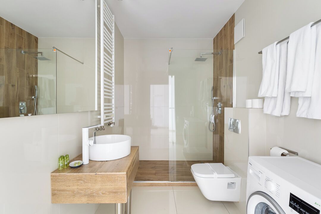 A modern bathroom with a wooden vanity, a glass shower enclosure, a toilet, and a washing machine.