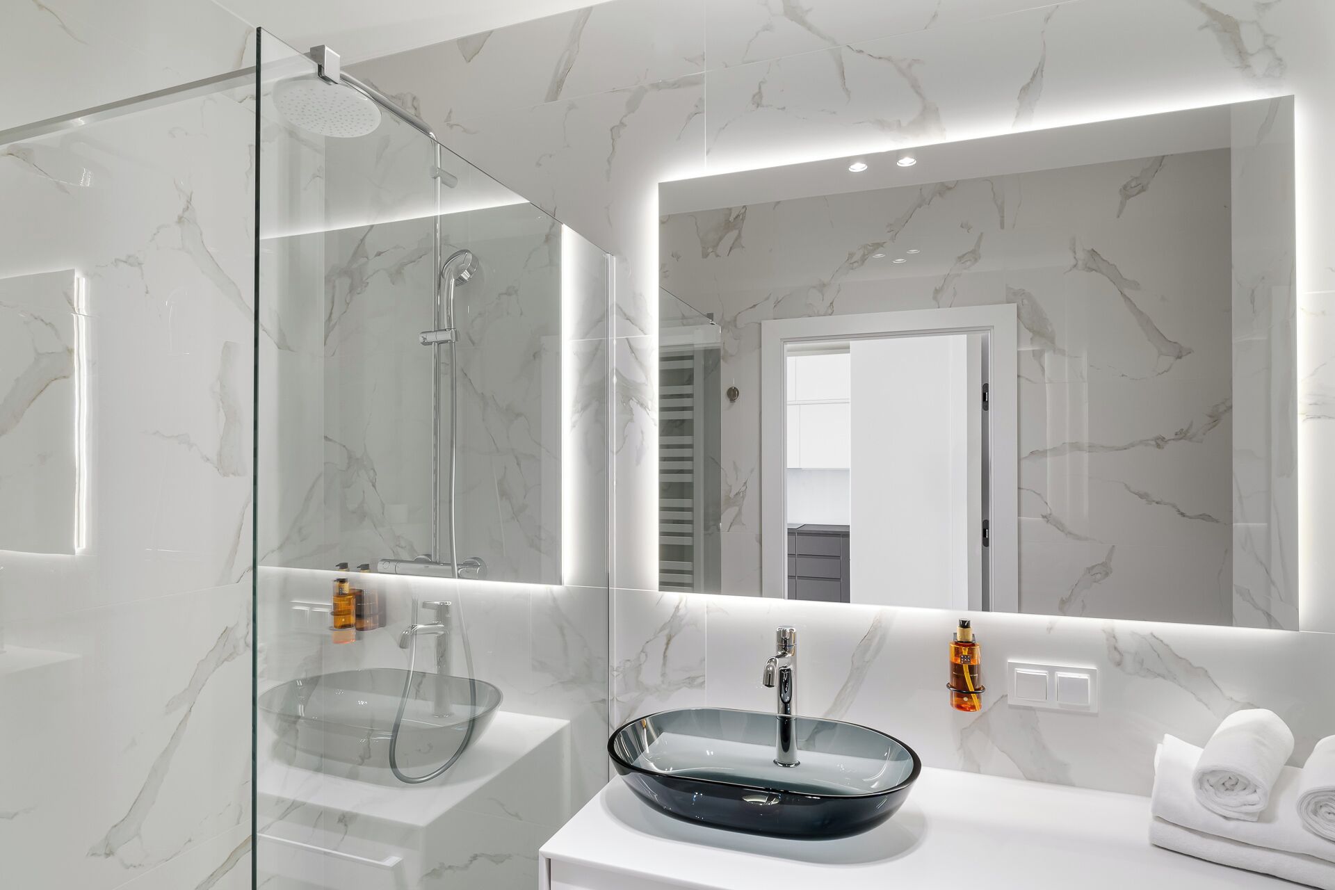 Une salle de bain moderne avec une douche à l’italienne en verre, un lavabo noir sur pied et un grand miroir au-dessus du lavabo.