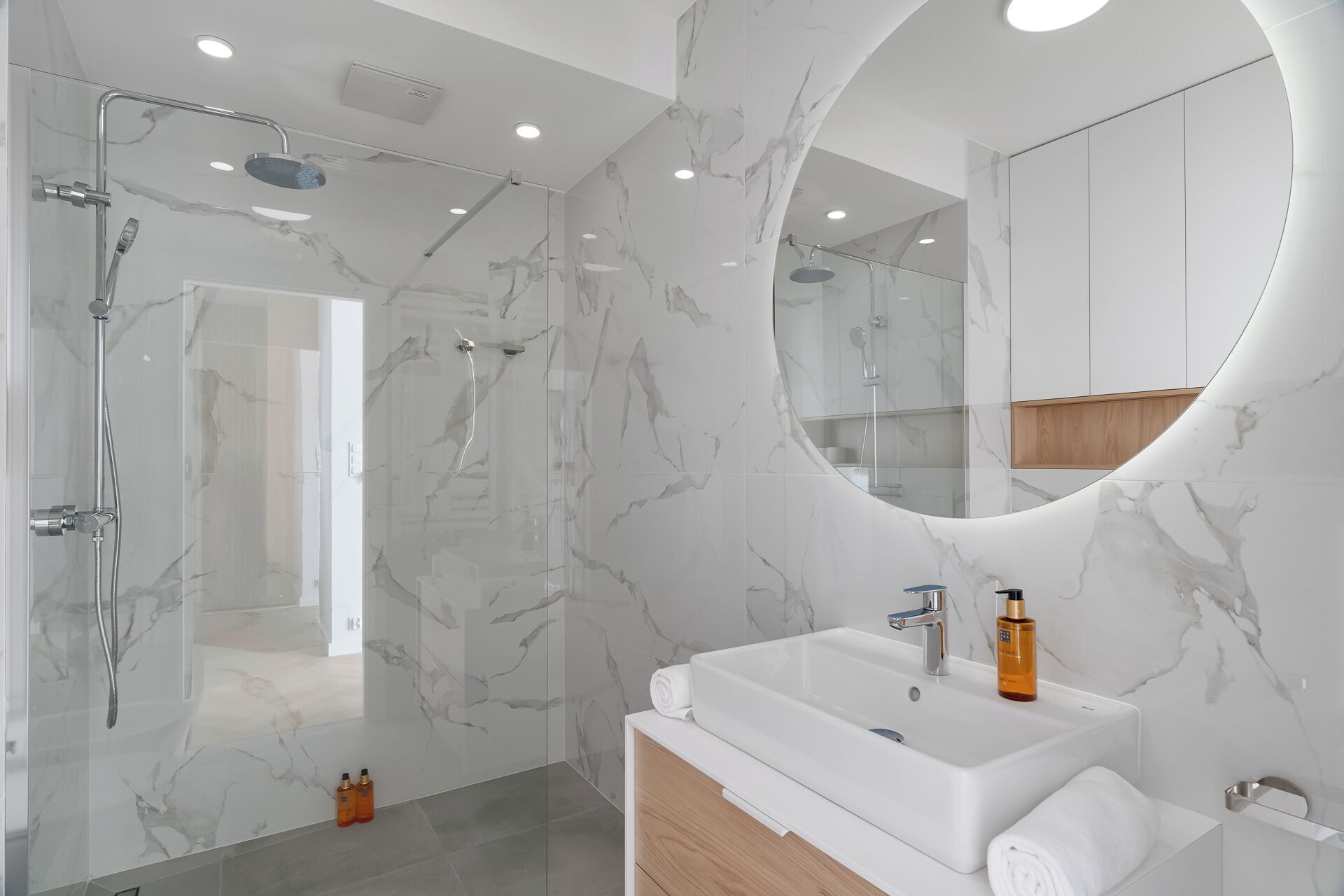 A modern bathroom with a glass-enclosed shower, a large mirror, and a white sink with toiletries.