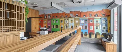A reception desk with a wooden counter, a plant, and a view of colorful buildings through a window.