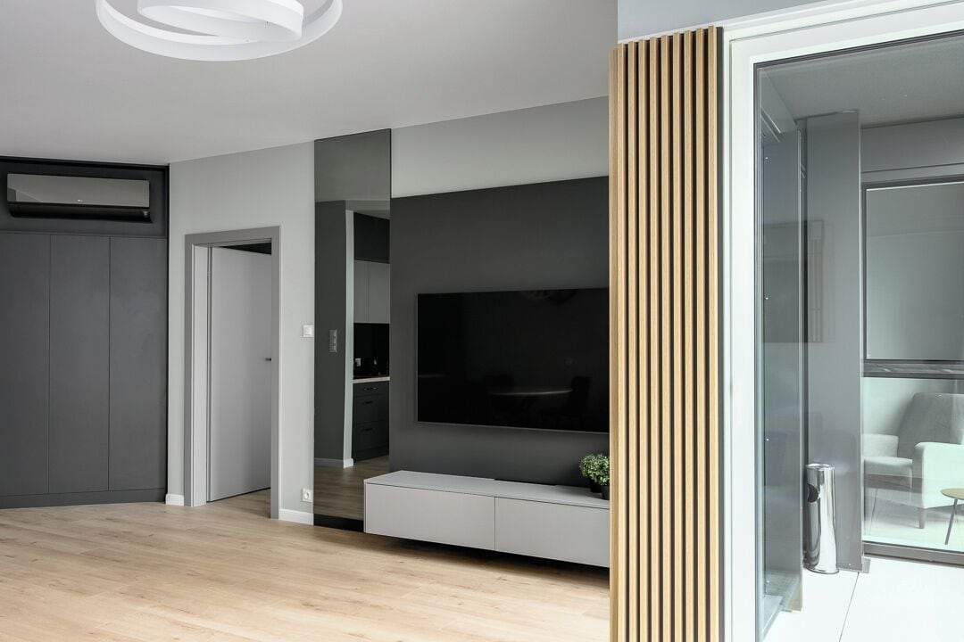 Un moderno salón con televisor de pantalla plana, mueble empotrado de entretenimiento y puerta corredera de vidrio que da a un balcón.
