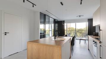 A modern kitchen with a wooden island, large windows, and a view of the outdoors.