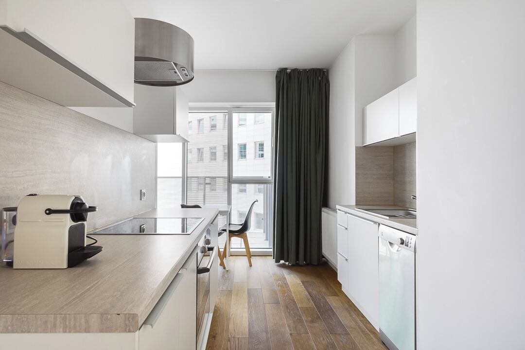 A modern kitchen with a built-in oven, a coffee machine, and a window with curtains.
