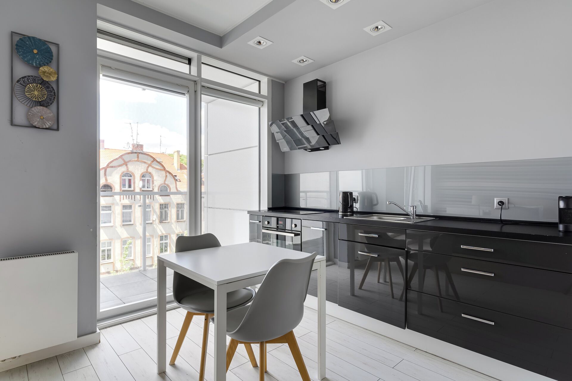 A modern kitchen with a dining area, large windows, and a view of buildings outside.