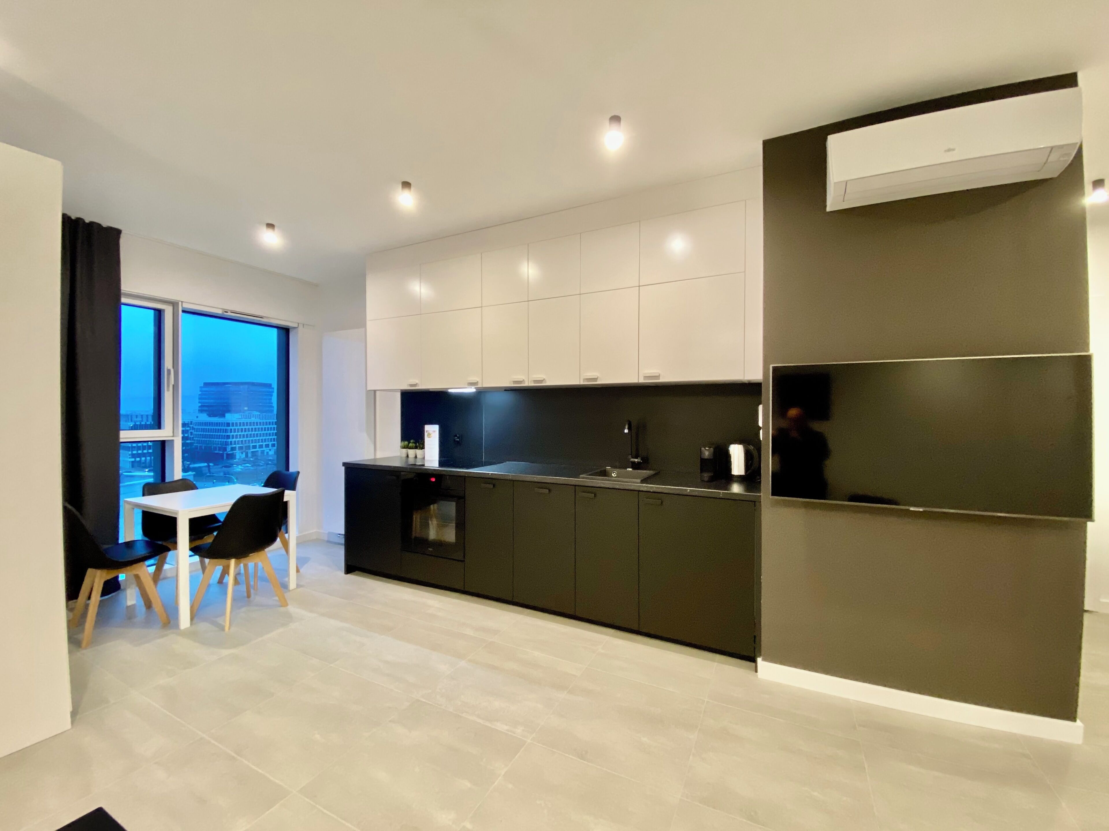 A modern kitchen with a dining area, featuring a large window, a built-in oven, and a black countertop.
