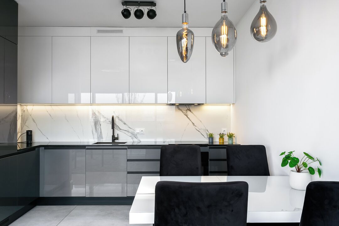 Una cocina moderna con armarios blancos, encimera de mármol e iluminación colgante.