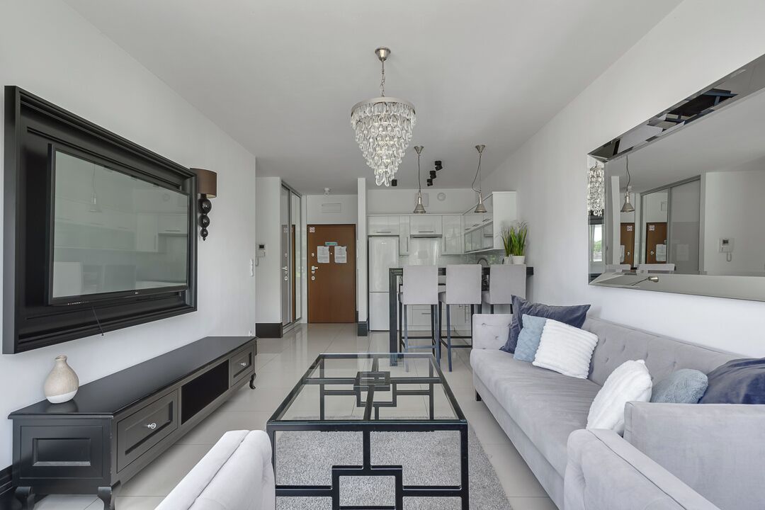 Ein modernes Wohnzimmer mit einem großen Flachbildfernseher, einem Glastisch, einem grauen Sofa und einer Kristallleuchtre.