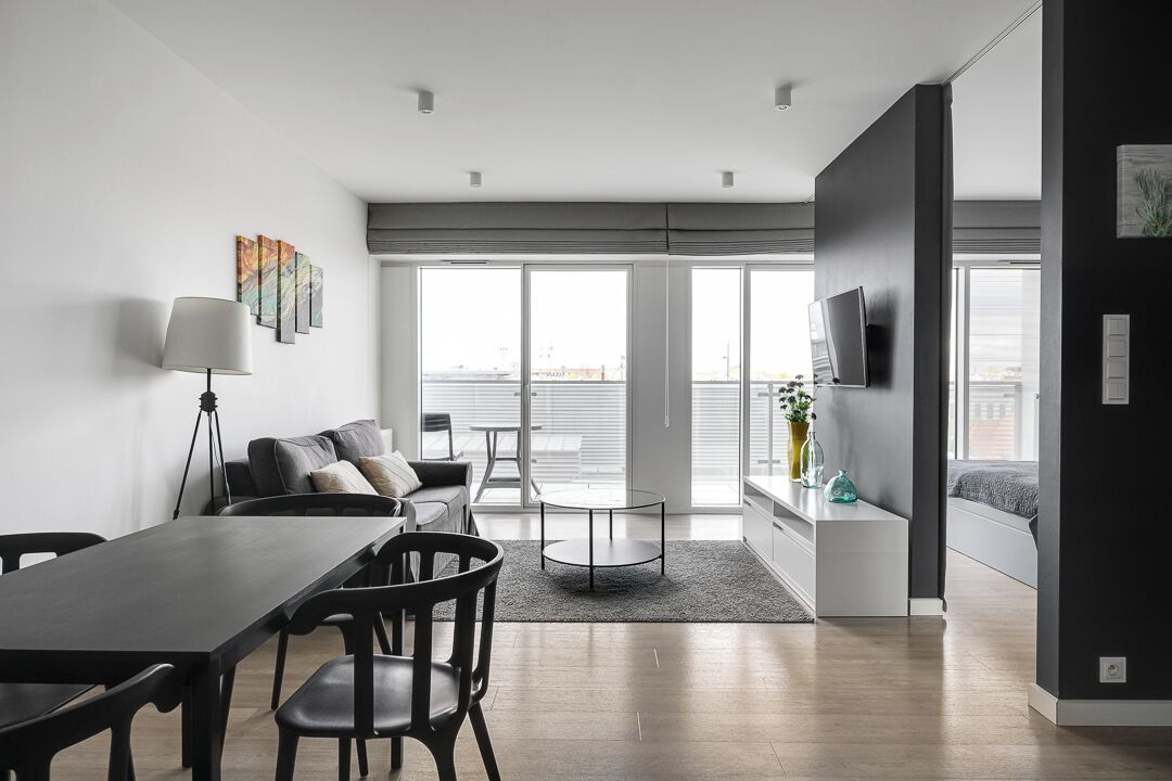 Uma sala de estar moderna com área de jantar, janelas amplas e uma TV de tela plana na parede.