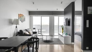 Uma sala de estar moderna com área de jantar, janelas amplas e uma TV de tela plana na parede.