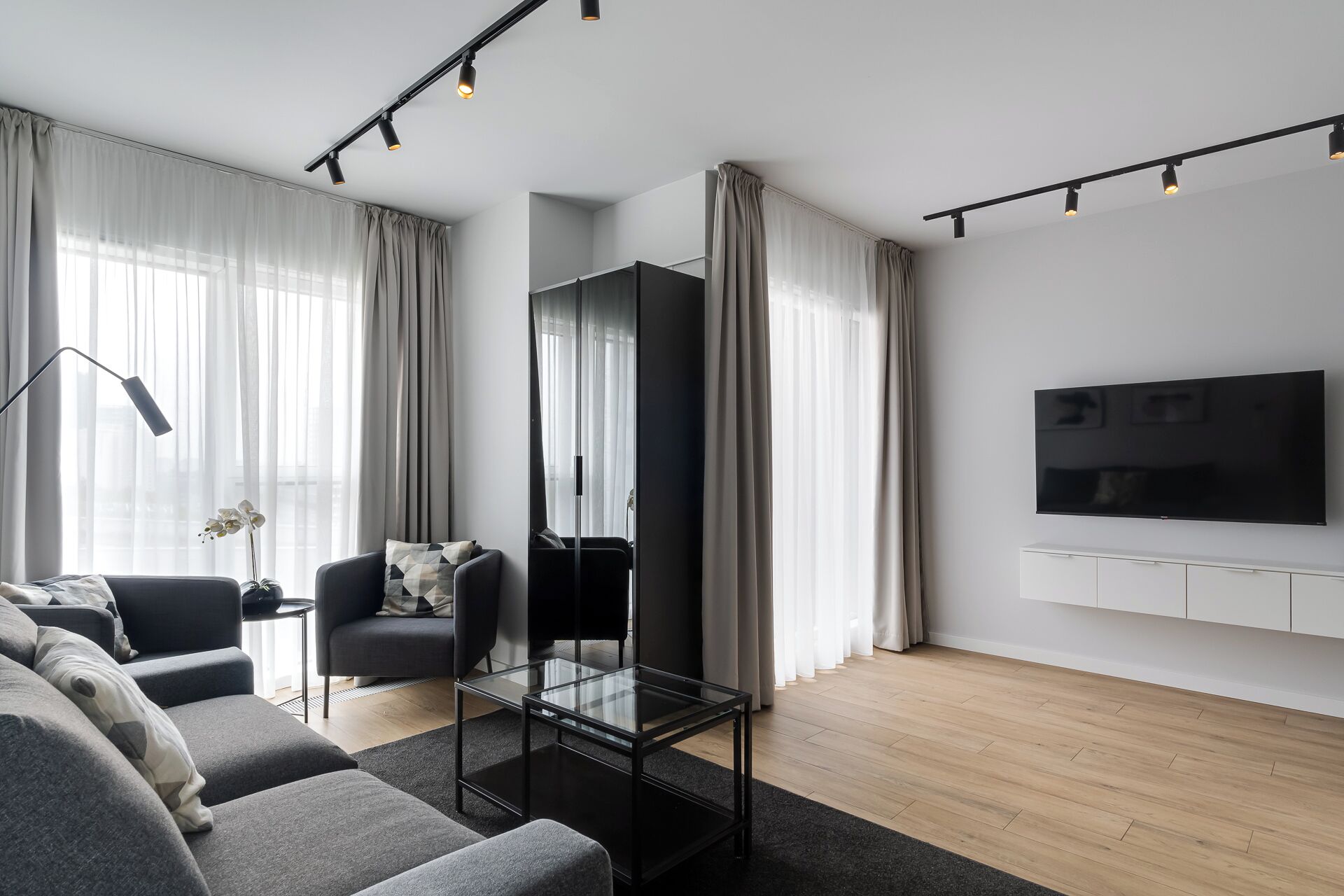 Una sala de estar moderna con sofá, sillón, mesa de centro de vidrio y televisor de pantalla plana montado en la pared.