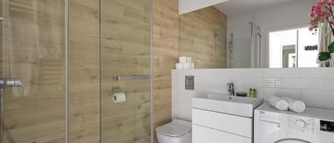 Un baño moderno con pared de madera, cabina de ducha de cristal, inodoro, lavamanos y lavadora.