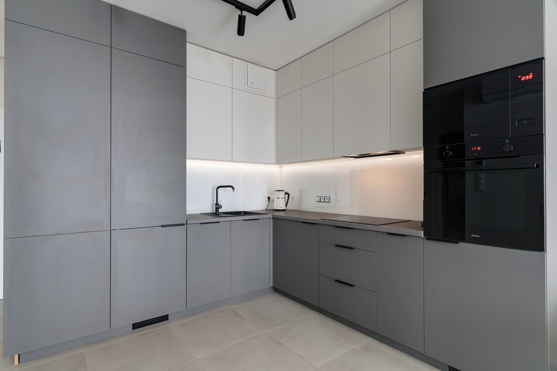 A modern kitchen with grey cabinets, a black refrigerator, and a built-in oven.