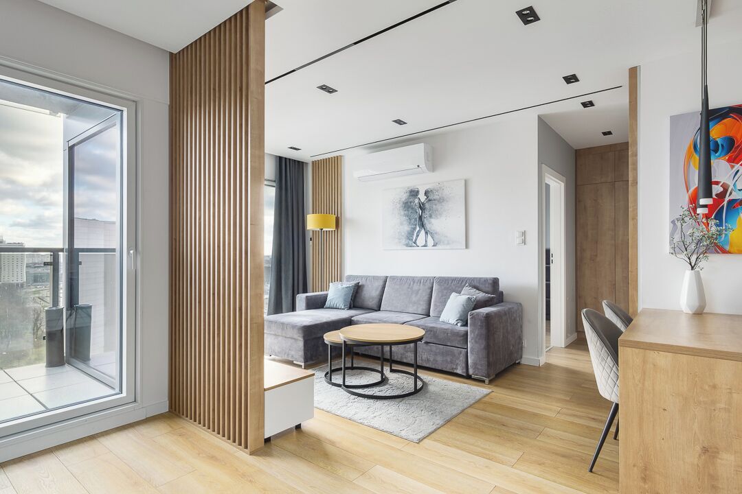 Ein modernes Wohnzimmer mit grauem Sofa, rundem Couchtisch und einer Holzwand.