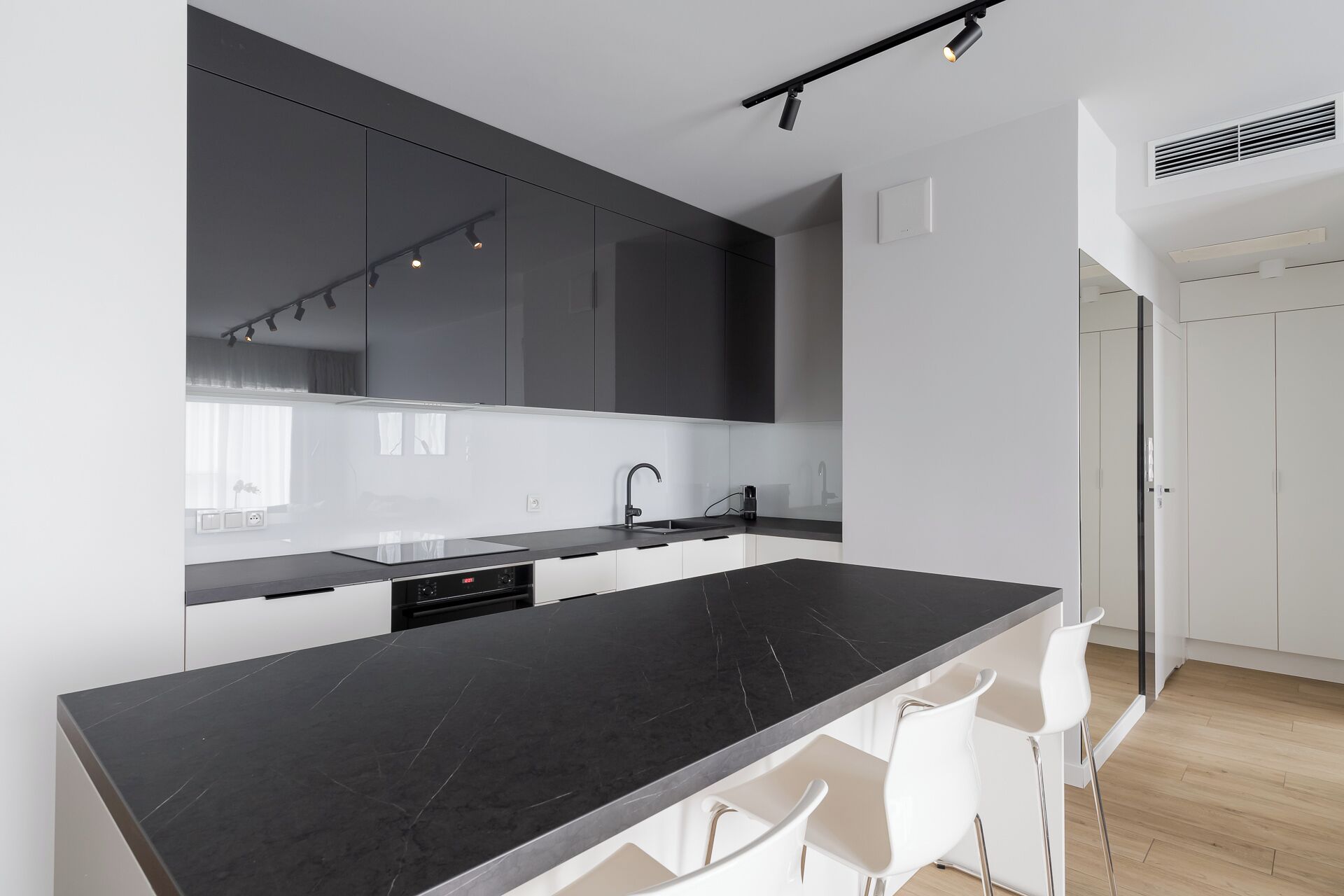 Una cocina moderna con encimera de mármol negro, sillas blancas y armarios oscuros.