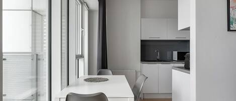 A modern kitchen with white cabinets, a microwave, and a coffee maker. There is a dining area with a white table and chairs.