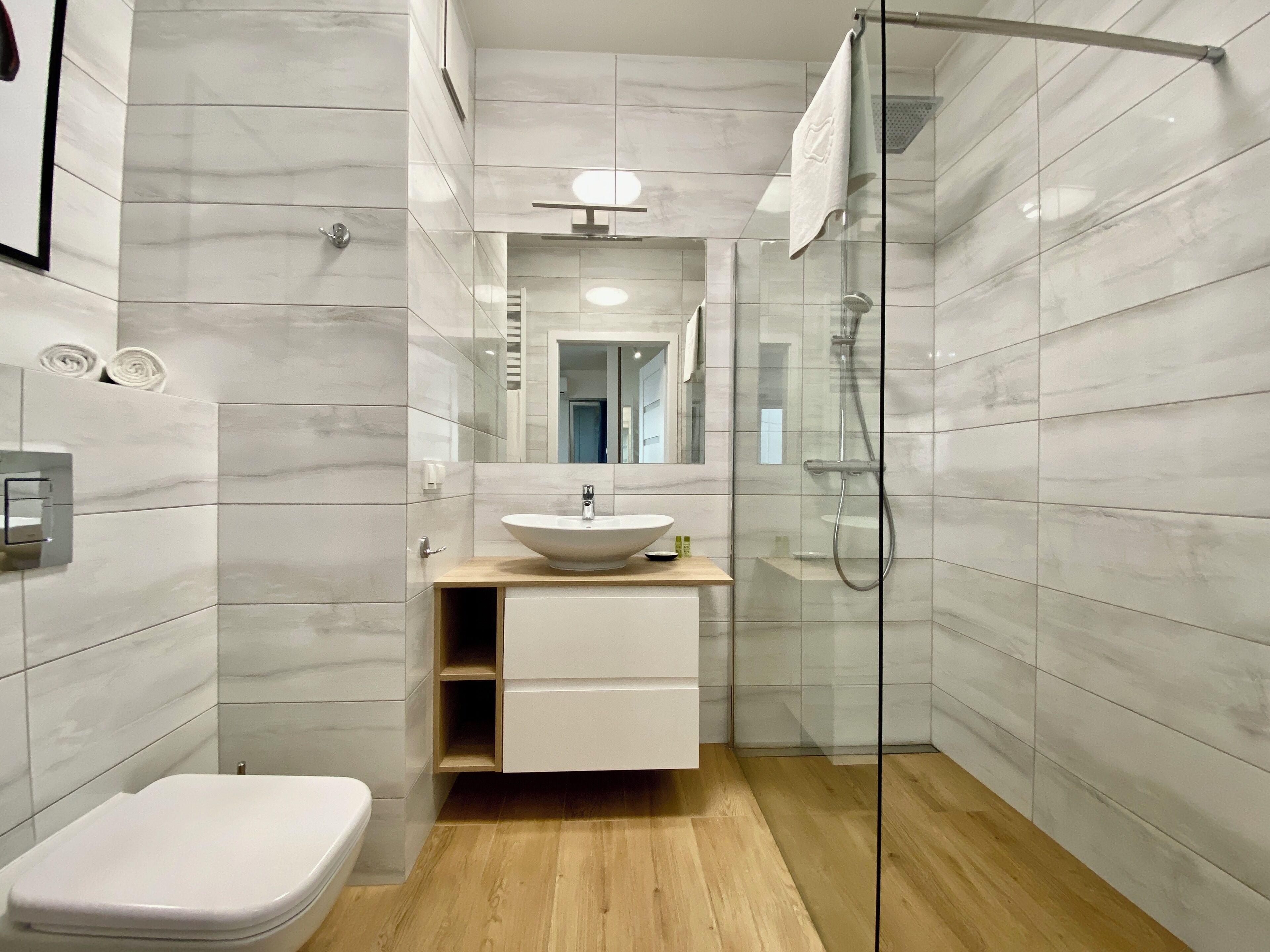 Een moderne badkamer met een wit toilet, een wastafel met een marmeren blad en een douchecabine van glas.