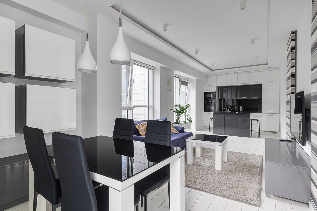 Une cuisine moderne avec des meubles blancs, un coin repas avec une table et des chaises noires, et un salon avec un canapé et une table basse.