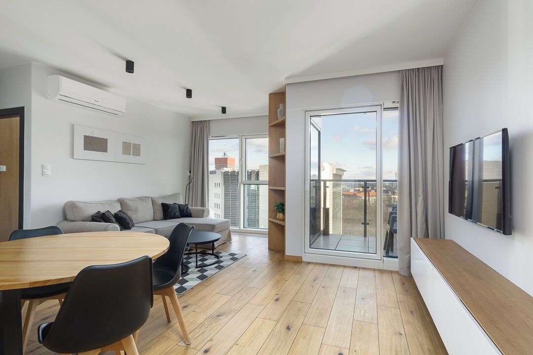 Una sala moderna con comedor, un sofá, un televisor y un balcón con vista a la ciudad.
