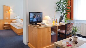 A hotel room with a bed, a desk with a television, a lamp, a coffee maker, and a chair. - Hotel Villa Subklew (Sellin)