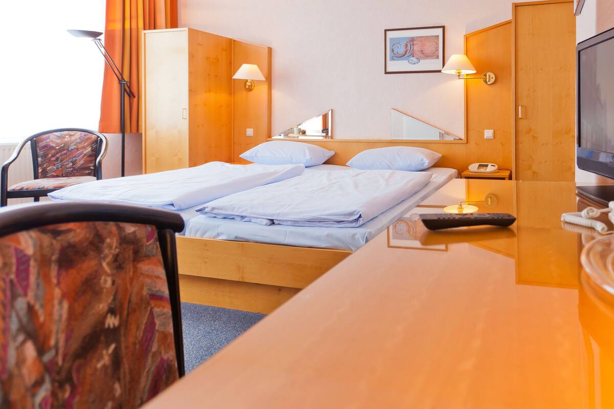 A hotel room with two beds, a desk, a chair, a TV, and a minibar.