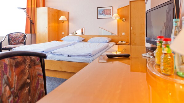 A hotel room with two beds, a desk, a chair, a TV, and a minibar. - Hotel Villa Subklew (Sellin)