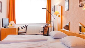 Una habitación de hotel con dos camas, un escritorio con una computadora, una silla y una lámpara.